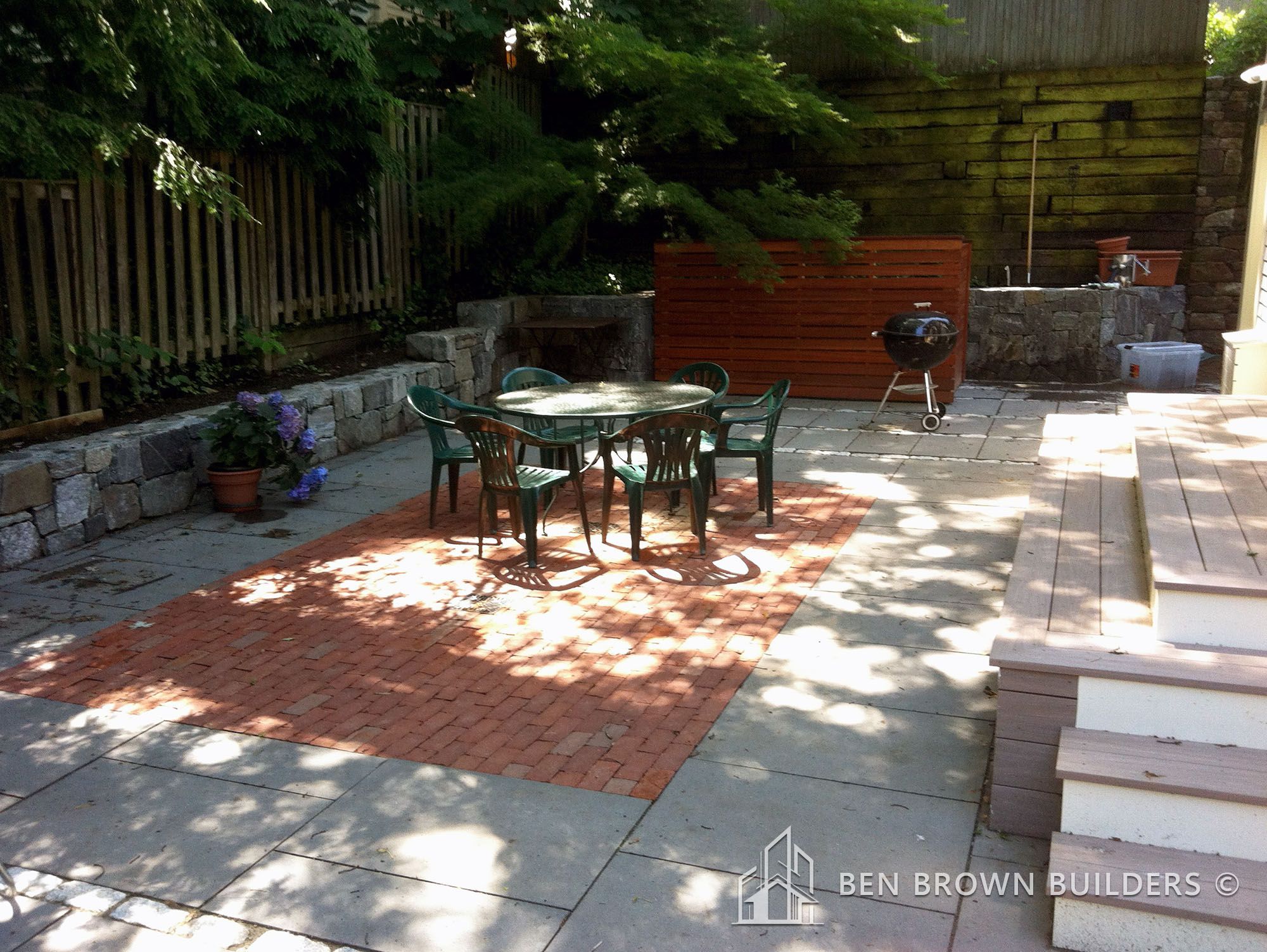 Backyard patio area with brick flooring, outdoor furniture set, grill, and a surrounding wooden fence