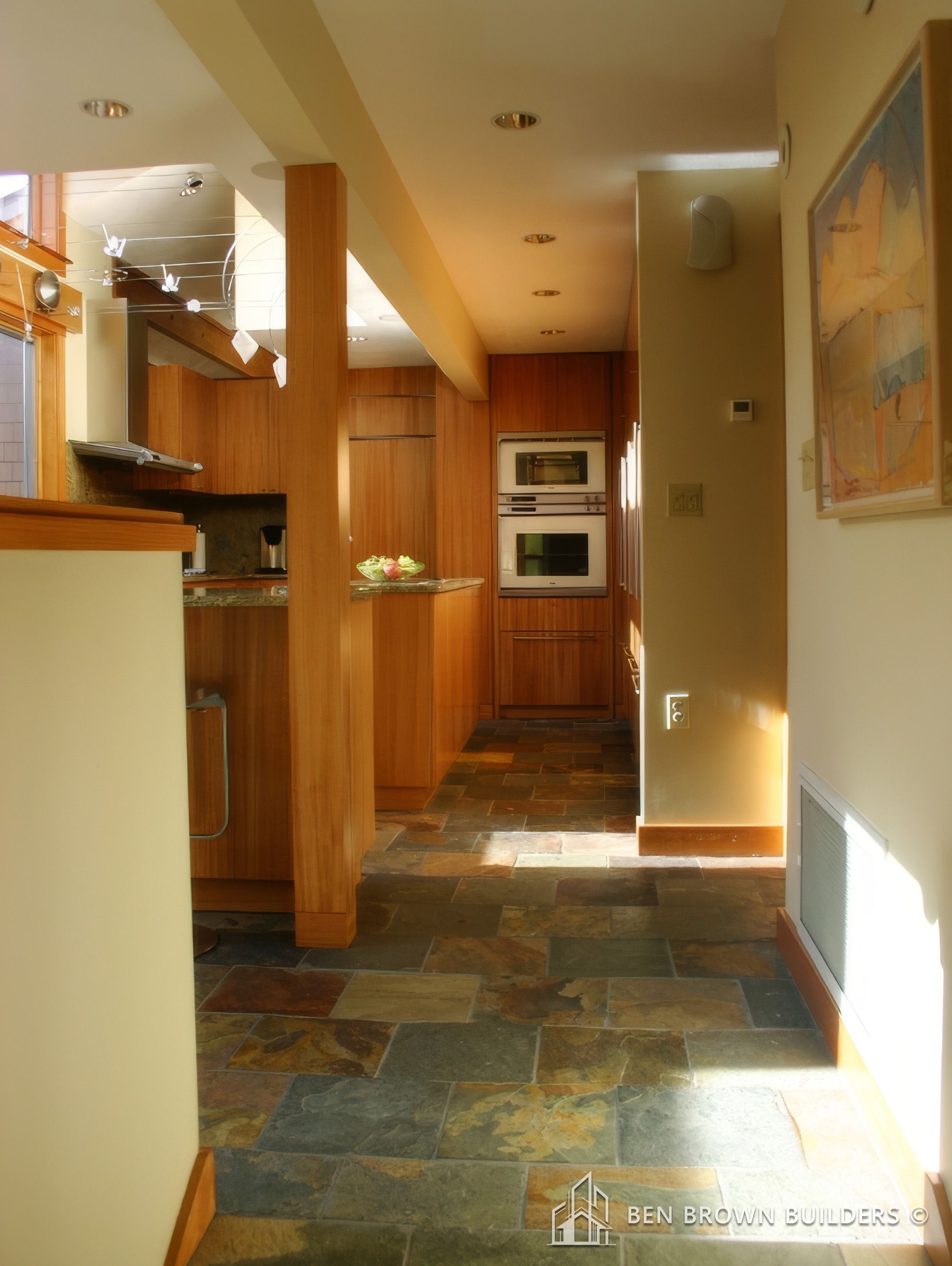 Modern kitchen interior with wooden cabinets, built-in appliances, and multicolored slate tile flooring