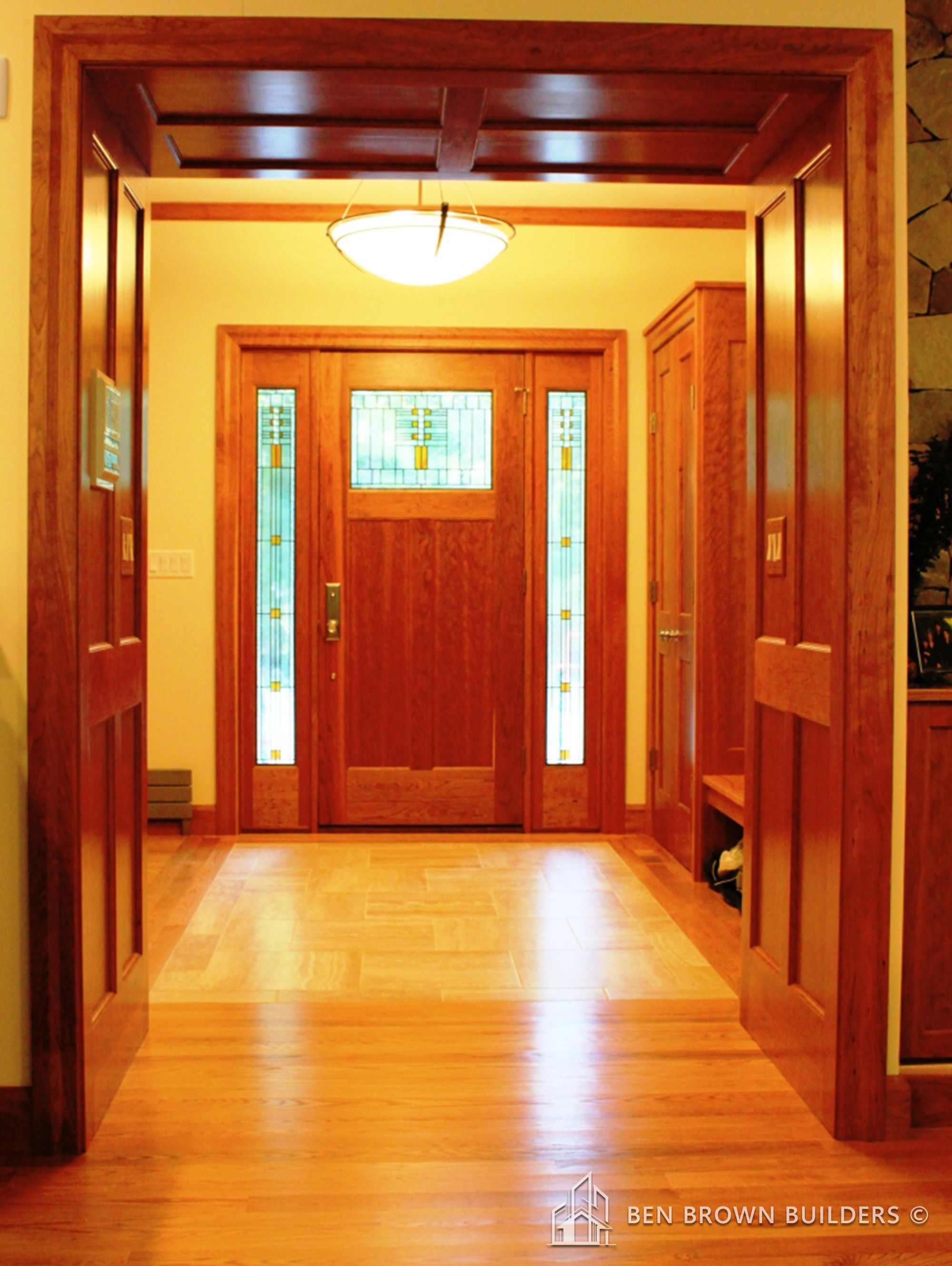 Warm entryway with a wooden front door featuring stained glass, hardwood floors, and a hanging light fixture