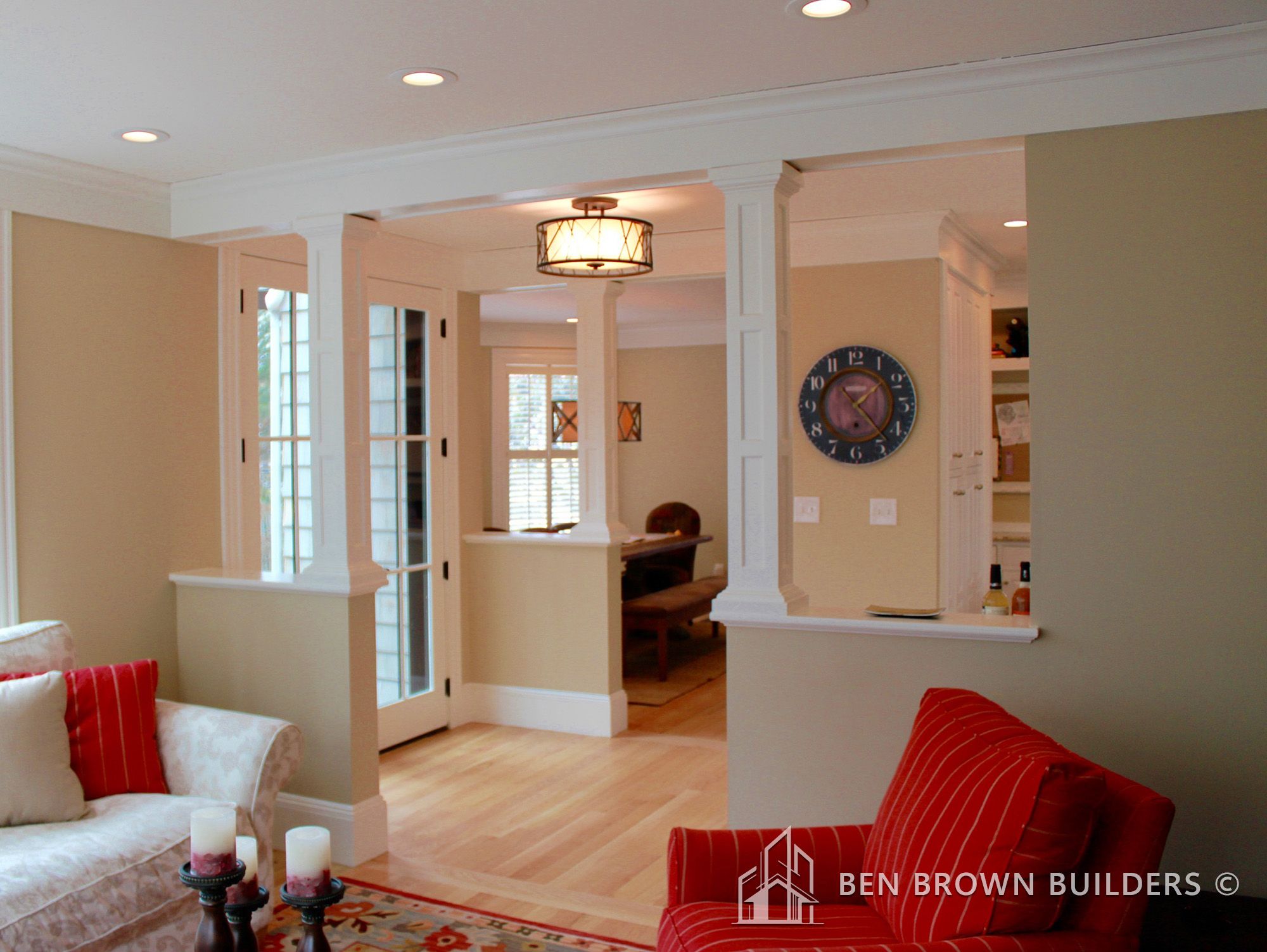 Inviting living space with white columns, French doors, cozy seating, and a large wall clock creating a homey atmosphere.