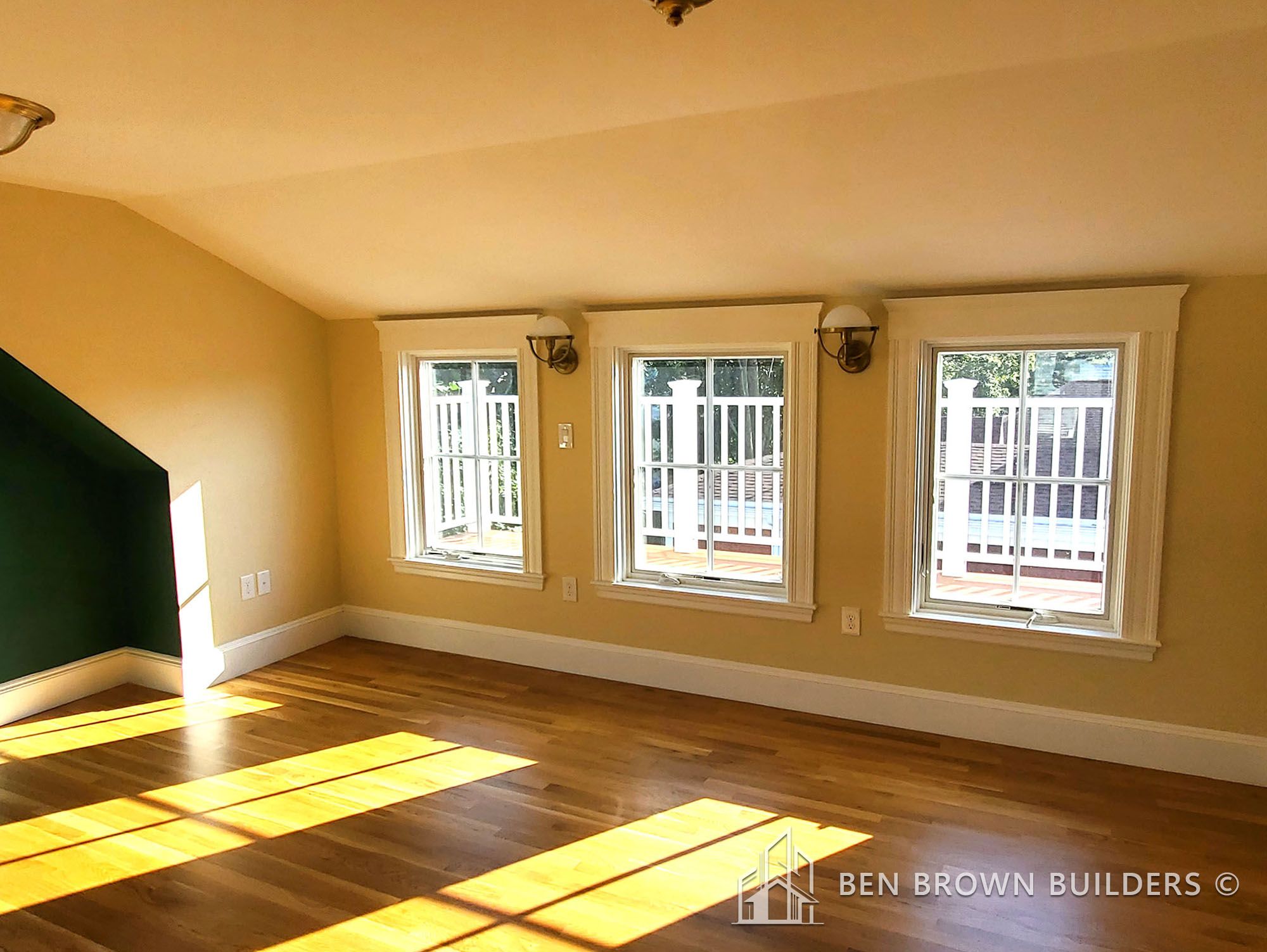 Bright room with a green accent wall, multiple windows leading to a balcony, and hardwood flooring