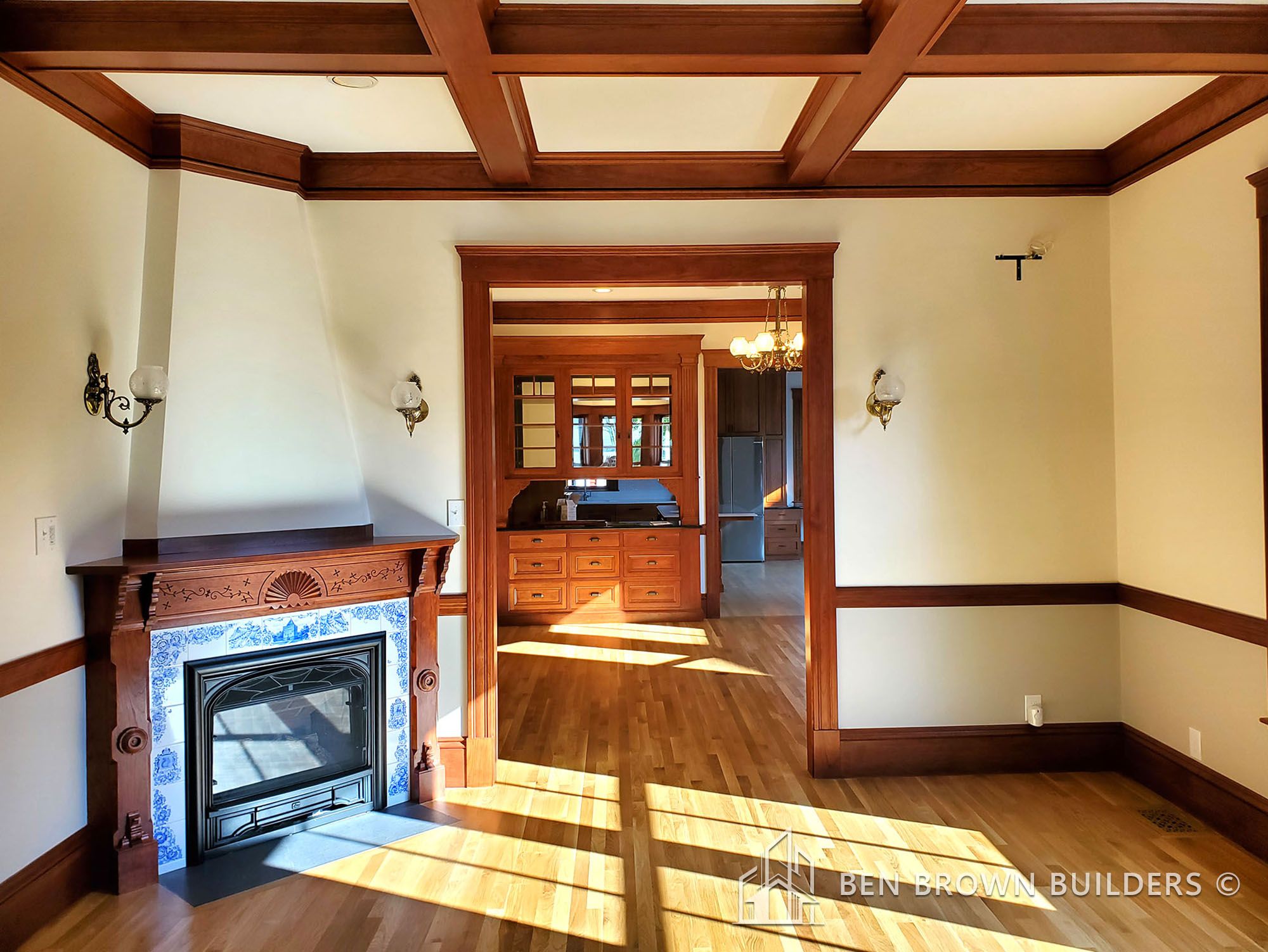 Spacious room with hardwood flooring, a fireplace with ornate blue tiles, and wooden coffered ceilings