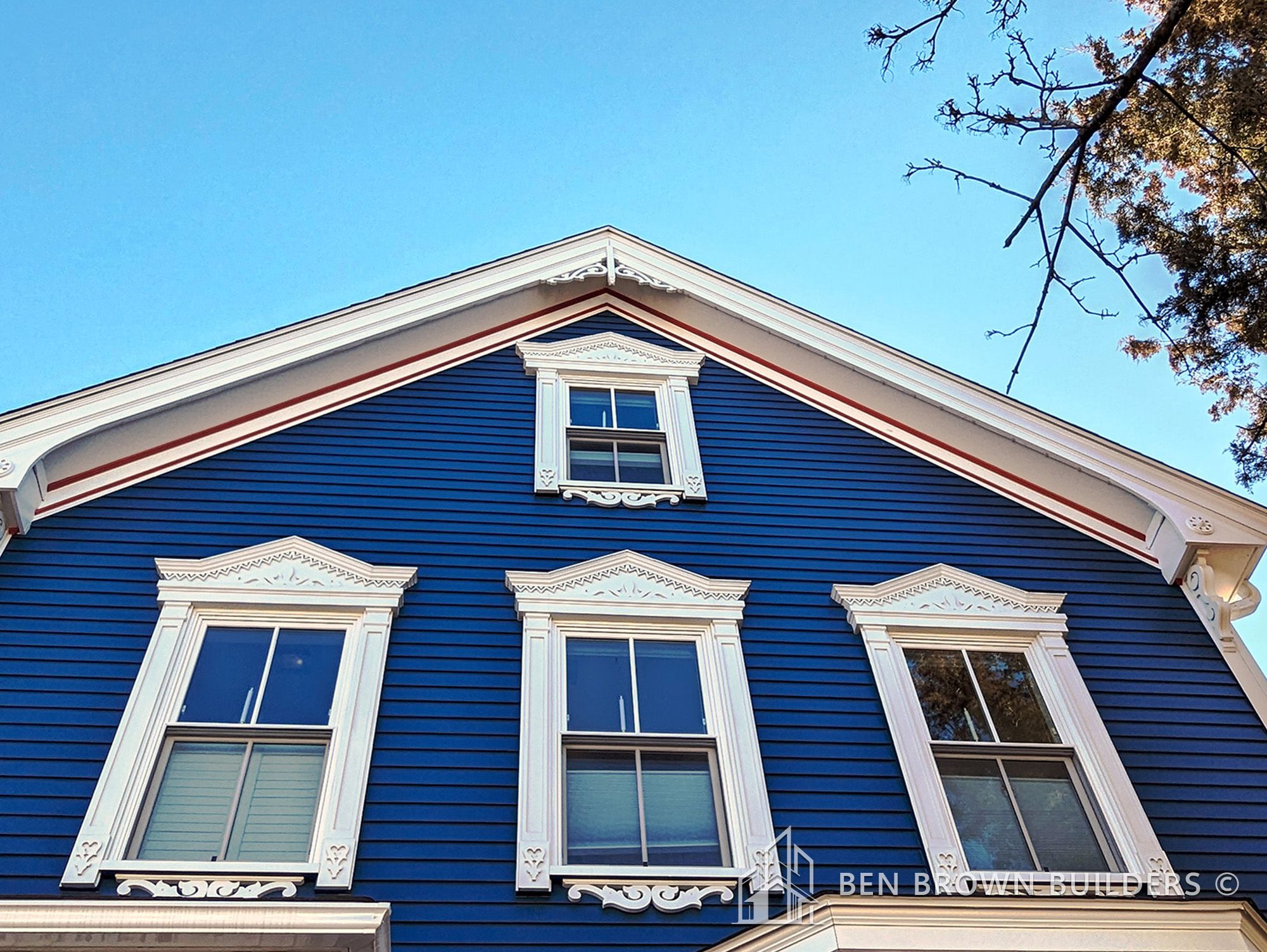 Close-up of a blue Victorian house with white trim and decorative gable brackets under a clear sky.