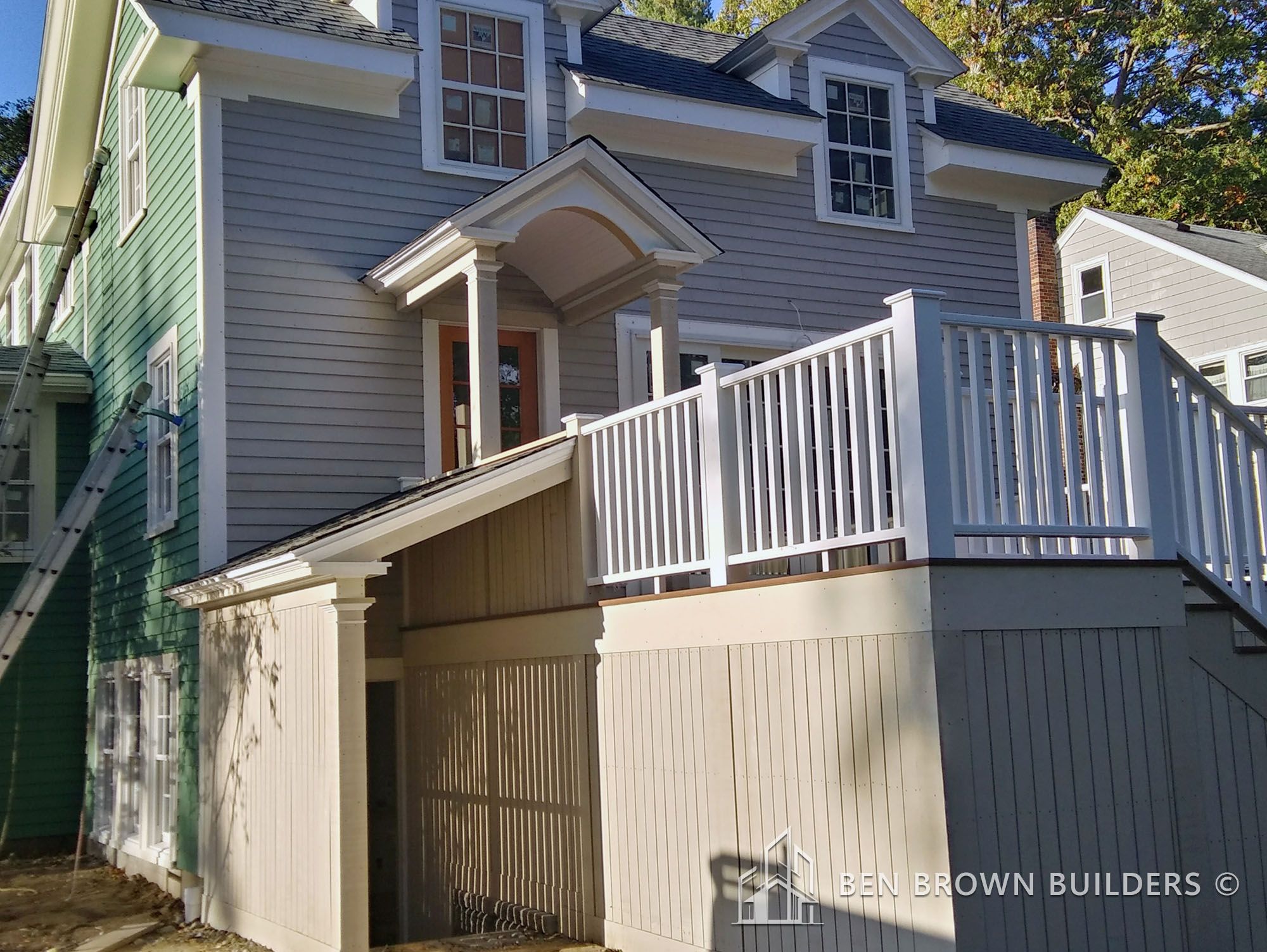 Newly constructed home entrance with a wooden stairway and porch, neutral siding, and a contrasting green neighboring house.